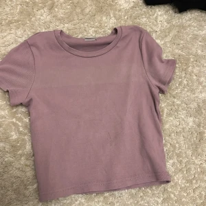 Ljuslila ribbad topp från Lindex - En enkel och snygg ljuslila ribbad topp från Lindex. Modellen är croppad med korta ärmar och rund halsringning. Perfekt att matcha med jeans eller kjol för en chill look.