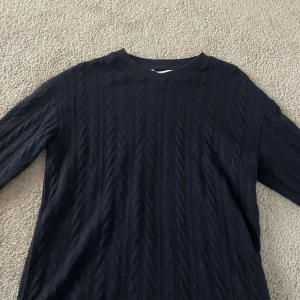 Mörkblå stickad tröja från Hm - Mörkblå stickad tröja med klassiskt kabelstickat mönster och rund halsringning. Tröjan har långa ärmar och en tidlös look som passar perfekt till jeans eller kjol. Mjuk och skön känsla, perfekt för kyligare dagar.