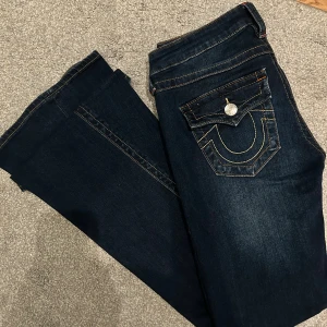 True Religion low bootcut jeans - Snygga mörkblåa true religon joey jeans som sitter lågmidjat. Se deftekter bild 4+5. Mått:- lapp 26  - Midja tvärs över 38 cm  - Innebenslängd 82 cm  - Midjehöjd 19 cm  - Benvidd längts ned 26,5 cm  - Stretchigt material vilket är bekvämt!💕