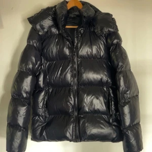 Svart pufferjacka med huva - Säljer nu min puffer jacka då den är lite för stor för mig. Har stått i garderoben sen vintras då jag bara hade på mig den några gånger. Men den är riktigt bra på att hålla värmen och stå emot vinden. Med en stor luva som inte förstör håret varje morgon. (Storleken är XS men passar även S)