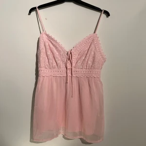 Ljusrosa spetstopp från Vero Moda - Supersött ljusrosa linne från Vero Moda med tunna axelband, spetsdetaljer och knyt framtill. Toppen har broderad överdel och är perfekt att styla med tex vita jeans. super söt, aldrig använd då jag själv inte tycker ja passar i rosa. säljs för att den inte används🙌🏻🩷
