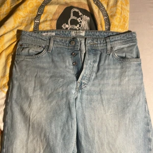 Ljusblå jeans från Jack & Jones 32/34 - Säljer ett par ljusblå jeans från Jack & Jones i klassisk femficksmodell. Jeansen har raka ben, knappgylf och snyggt läderpatch bak i midjan. Perfekta för dig som gillar en avslappnad och tidlös look.