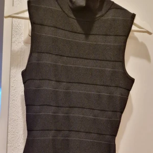 Svart kort klänning från Mango - Snygg svart kort klänning från Mango i storlek S. Klänningen är ärmlös med en tight passform och har horisontella ränder i materialet. Den har en liten ståkrage och dragkedja bak. Perfekt för dig som gillar stilrena och moderna plagg.