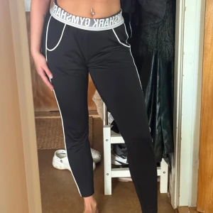 Svarta Gymshark joggers med vita detaljer - Svarta joggers från Gymshark med vita kontrastdetaljer längs sidorna och fickorna. Hög midja med bred resår och Gymshark-logga. Slimmad passform i mjukt, stretchigt material. Perfekta för träning eller chill.