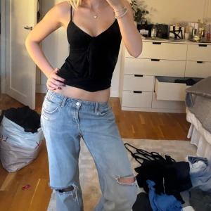 Fest topp - Säljer ett svart linne i mjuk sammet med smala axelband och snygg knytning framtill. Toppen har en djup v-ringning och croppad passform som ger en trendig look. Perfekt att styla med jeans eller kjol för en cool vibe.