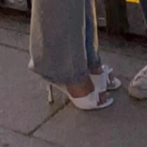 Vita klackade sandaler med rosett - Säljer ett par vita sandaler med smal klack och öppen tå. Skorna har en snygg rosettdetalj framtill och en stilren design som passar till jeans eller klänning. Tillverkade i syntetmaterial med en elegant och modern look.