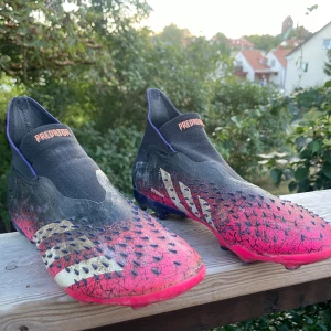 Adidas Predator Pro fotbollsskor svart/rosa - Säljer ett par Adidas Predator Pro fotbollsskor i svart och rosa med lila detaljer och silvriga ränder med ”demonskinn”. Gummifjäll som sticker ut och ger extra skruv på bollen. Perfekta för dig som vill utmärka sig på planen. Jättedyra i inköpspris. 