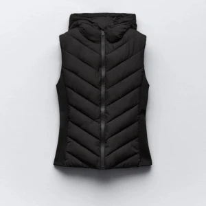 Svart dunväst från Zara - Svart dunväst från Zara med huva och dragkedja framtill. Västen har en figurnära passform och är perfekt för lager-på-lager-stil. Pris går att diskutera💕