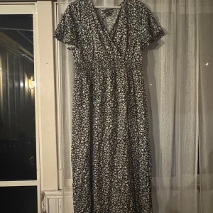 Blommig långklänning från SHEIN - Supersöt långklänning från SHEIN i svart med vitt blommönster. Klänningen har v-ringning, korta ärmar och smockad midja som ger en snygg passform. Perfekt för dig som gillar en flowy och feminin stil.