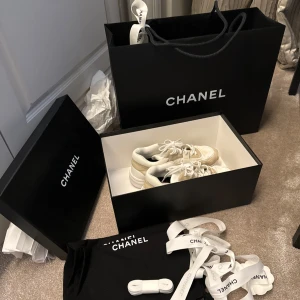 Chanel sneakers beige/vita strl 37 - Exklusiva Chanel sneakers från Collection Métiers d’Art 2022 i beige och vitt. Snygg chunky sula, rund tå och klassisk snörning. Kommer med originalkartong, dustbag och extra skosnören. Perfekta för dig som vill ha en lyxig och trendig look. Kvittot finns