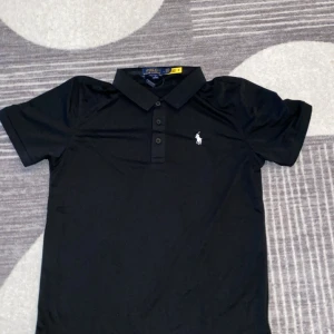 Svart pikétröja från Polo Ralph Lauren - Svart pikétröja från Polo Ralph Lauren med klassisk krage, tre knappar och den ikoniska broderade loggan på bröstet. Tillverkad i 100% bomull för en skön och luftig känsla. Perfekt för en clean och stilren look. Ska du åka på semester under de kommande kalla månader så är denna tröja perfekt för dig. Pris kan diskuteras vid snabbaffär!!