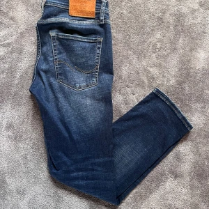 Jack & Jones Jeans *28/30* - Snygga mörkblå jeans från Jack & Jones i klassisk femficksmodell. Jeansen har en lätt tvättad look med slitningar framtill och bakfickor med dekorativ söm. Har en ”Regular Fit” passform i modellen ”Clark”.