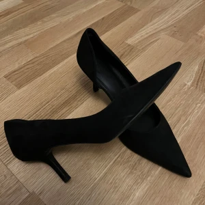 Svarta pumps med spetsig tå från H&M - Svarta pumps från H&M i storlek 39. Skorna har en elegant spetsig tå, smal klack och är klädda i mockaliknande material. Perfekta för dig som gillar en klassisk och stilren look med lite edge.