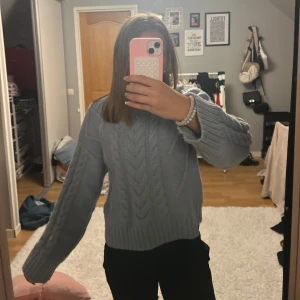 Ljusblå stickad kabeltröja - Supermysig ljusblå stickad tröja med kabelstickat mönster och breda ribbade muddar. Rund halsringning och långa ärmar. 