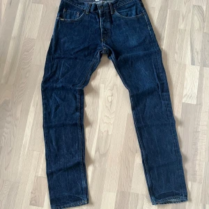 Mörkblå jeans från Tiger of Sweden - Snygga mörkblå jeans från Tiger of Sweden med klassisk femficksdesign och raka ben. Jeansen har orange kontrastsömmar och detaljerade nitar. Tillverkade i slitstarkt denim för en tidlös look.