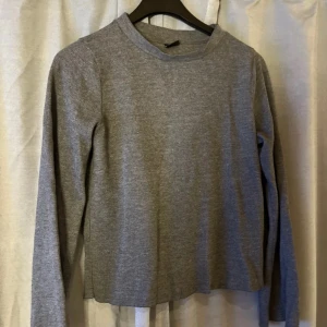 Grå långärmad tröja från Gina Tricot - En basic grå långärmad tröja från Gina Tricot i storlek XS. Tröjan har en enkel rak passform och rund halsringning. Perfekt att matcha med jeans eller kjol för en clean look.