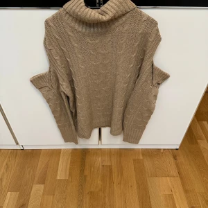 Beige stickad polotröja med kabelmönster - Beige stickad polotröja med grovt kabelstickat mönster och bred polokrage. Tröjan har lång ärm och ribbade muddar vid ärmslut och nederkant. 