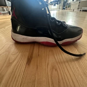 Nike Air Jordan 11 Retro svart/röd bred - Säljer ett par Nike Air Jordan 11 Retro med svart ovandel i skinn och textil, lackade detaljer och röd sula. Klassisk Jumpman-logga i rött på hälen och snörning framtill. Perfekta för dig som gillar ikoniska sneakers med streetstyle-vibe. Anledningen är för att de är för skorna är för små så det är därför jag säljer de. Jag köpte skorna på sneakerhyllan för 2300 kr. Kan antingen frakta eller mötas i verkligheten. Om ni känner att ni vill köpa i verkligheten blir det lite billigare.