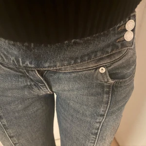 Weekday Millennial jeans låg midja - Säljer ett par blå Weekday Millennial jeans i storlek 26. De har låg midja, utsvängda ben och klassisk femficksdesign. Jeansen är i denim med snygg tvätt och har dubbla knappar i midjan. Perfekt för dig som gillar 00-talsvibbar och en avslappnad look. Jag har storlek 36