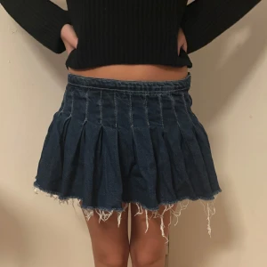 Mörkblå plisserad jeanskjol från Zara - Superfin mörkblå jeanskjol från Zara med plisserad design och rå, fransig kant nertill. Kjolen har dragkedja bak och sitter snyggt i midjan. Perfekt för dig som gillar en edgy och trendig look.