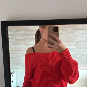 Röd offshoulder stickad tröja - Säljer en röd stickad tröja med offshoulder-modell och bred ribbad kant upptill. Tröjan har lång ärm och en loose fit, perfekt för dig som gillar en avslappnad men ändå snygg stil. Materialet är mjukt och skönt, och färgen är riktigt poppig röd.