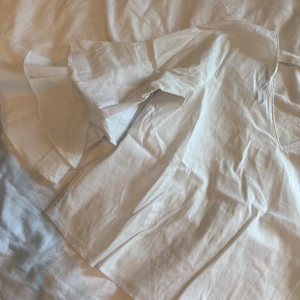 Vit omlottklänning från Zara Basic - Supersöt vit omlottklänning från Zara Basic med v-ringning och volangärmar. Klänningen är kort och har en feminin passform med knytband i midjan. Perfekt för sommarens alla tillfällen och tillverkad i mjuk bomull för en luftig känsla.