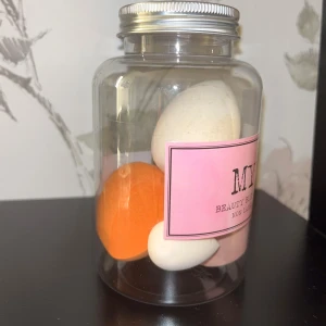 Beautyblenders i burk med lock - Säljer en burk med 4 stycken beautyblenders från MY. Innehåller olika former och storlekar, bland annat en orange och flera vita och rosa svampar. Perfekt för att applicera foundation, concealer eller puder. Burken har ett silvrigt skruvlock och rosa etikett.
