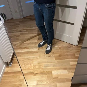 Mustang jeans slim fit - Säljer ett par blåa Mustang jeans med slim fit och klassisk femficksdesign. Jeansen har snygga kontrastsömmar och en liten röd tag på bakfickan. Modellen är smal och sitter tajt längs benen, perfekt för en modern look.