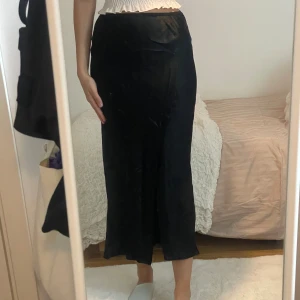 Svart långkjol i sammet med slits - Säljer en svart långkjol i mjuk sammet med en snygg slits på sidan. Kjolen har en rak passform och sitter högt i midjan. Perfekt för dig som gillar en stilren och elegant look.