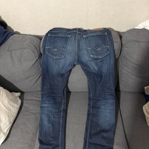 Replay Anbass - Snygga blå Replay Anbass jeans i slim fit med klassisk femficksdesign och coola slitningar. Jeansen har medelblå tvätt, kontrastsömmar och detaljerade bakfickor. Perfekta för dig som gillar en modern och stilren look.