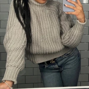 Grå stickad polotröja - Säljer en chunky grå stickad polotröja med breda ribbade muddar och hög hals. Tröjan har en loose passform och är perfekt för kyliga dagar. Den är mjuk och skön, och passar snyggt till jeans eller kjol.