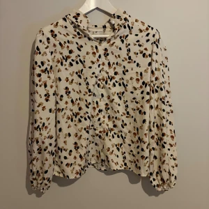 Mönstrad långärmad skjorta från SHEIN - Säljer en vit långärmad skjorta från SHEIN med coolt prickigt mönster i svart, brun och beige. Skjortan har elastiska ärmslut och en liten krage med knappdetalj. Perfekt för dig som gillar trendiga och bekväma plagg.