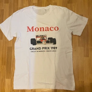 t-shirt med tryck - Snygg vit t-shirt med tryck från Monaco Grand Prix 1989. Framsidan har en stor formel 1-bil och texten 'Monaco Grand Prix 1989 Circuit de Monaco Monte Carlo' i rött och svart. Klassisk passform och rund hals, perfekt för motorsportfans.