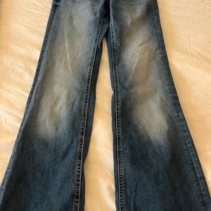 Blå bootcut jeans från Lindex - Snygga blå bootcut jeans från Lindex i klassisk tvättad denim. Jeansen har hög midja, vida ben och coola bakfickor med lock. Perfekta för dig som gillar retrovibbar och vill ha ett par jeans med riktigt skön passform.