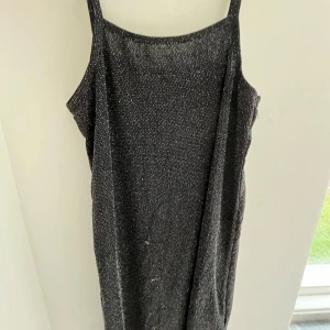 Glittrig svart klänning med smala axelband - Supersnygg svart klänning med glittriga detaljer och smala axelband. Klänningen har en rak passform och är perfekt för dig som vill sticka ut. Materialet känns mjukt och följsamt, och den glittriga ytan ger en extra touch till looken.