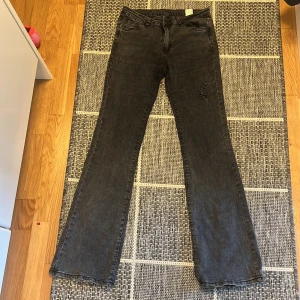 Svarta bootcut jeans från Gina Tricot - Snygga svarta jeans från Gina Tricot med bootcut-modell. Jeansen har klassisk femficksdesign, bälteshällor och en lätt tvättad look. Perfekta för dig som gillar en retrovibe och vill ha ett par jeans med lite vidare ben nertill.