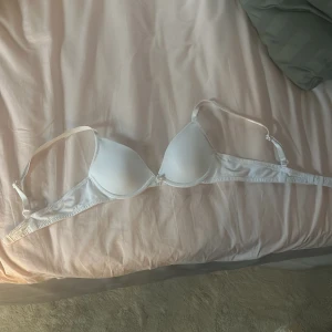 Vit vadderad bh med rosett - Säljer en enkel och stilren vit bh med bygel.  Har du klippt av lappen där det står vad den kommer ifrån bhn har en gulle liten rosett i mitten. Kosta 129 kr som ny