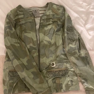 Camouflagejacka med nitar från Pulz Jeans - Snygg camouflagejacka från Pulz Jeans med dragkedja framtill och coola svarta nitar på båda ärmarna och fickorna. Jackan har militärgrön bas, raka linjer och detaljer 💗 storlek L men sitter bra på mig som är 170!