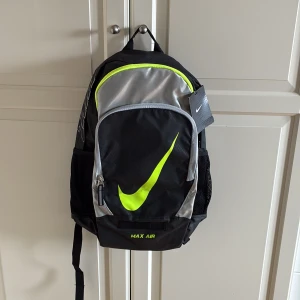 Ryggsäck från Nike Max Air - Nike Max Air ryggsäck i svart och silver med neongula detaljer och stor Swoosh-logga. Flera fack, meshfickor på sidorna och vadderade axelband. Finns datafack. Helt ny och etiketten sitter kvar. 