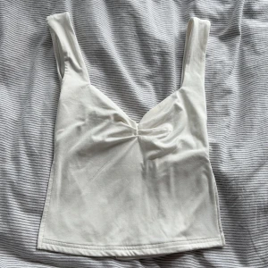 Vit croppad linnetopp med twist - Säljer en stilren vit linnetopp med breda axelband och snygg twistad detalj framtill vid bysten. Toppen är croppad och har en rak passform, perfekt att matcha med jeans eller kjol. Tillverkad i mjuk bomull för en bekväm känsla hela dagen. Toppen är köpt från TikTok-Shop förra sommaren, har enbart använt den 2 gånger. 