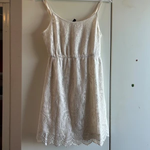 Vit spetsklänning från H&M Divided - Superfin vit kortklänning från H&M Divided med tunna axelband och vacker spets över hela klänningen. Klänningen har markerad midja och söt kant nertill. Perfekt för sommarens alla tillfällen!