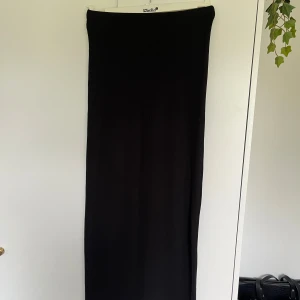 Svart ribbad långkjol - Säljer en svart långkjol med ribbad struktur. Kjolen har en rak och enkel design som ger en clean look. Perfekt att styla med sneakers eller boots.