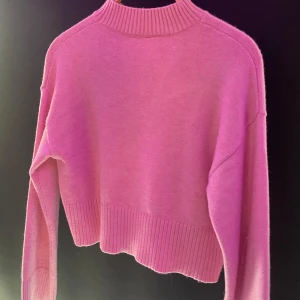 Rosa stickad tröja med ribbad kant - En söt rosa stickad tröja med hög ribbad hals och ribbade muddar vid ärmslut och nederkant. Tröjan har en loose passform och är perfekt för lager-på-lager under kyliga dagar.