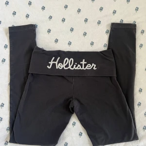 Mörkgråa leggings från Hollister XS - Mörkgråa leggings från Hollister med bred, vikt linning där Hollister-loggan är broderad framtill. Tight passform och stretchigt material som känns mjukt mot huden. Perfekta för en chill och sportig look. Ungefärliga platta mått:               över midjebandet: 34 cm               Innerbenslängd: 70 cm