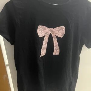 Svart t-shirt med spetsrosett  - Jättegullig t shirt med en rosa rosett på!!🎀🎀