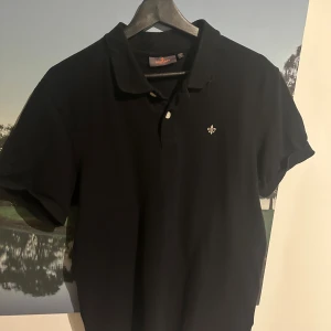 Svart pikétröja från Morris, M - Svart pikétröja från Morris med klassisk krage och två knappar framtill. Knappt använd så mycket fint skick. Vid frågor så får ni gärna höra av er!