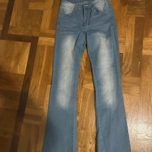 Blå bootcut jeans med detaljer - Snygga ljusblå jeans med bootcut-modell och slitningar framtill. Bakfickorna har coola silverfärgade nitar och dekorativa sömmar. Klassisk femficksdesign och normal passform. Perfekta för dig som gillar en retroinspirerad look.