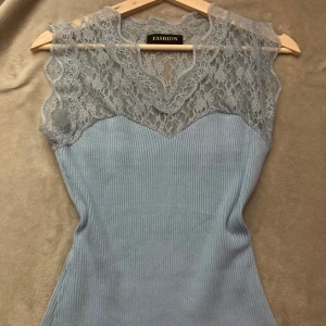 Ljusblå ribbad topp med spets - Supersöt ljusblå topp med ribbad kropp och transparent spets upptill. Toppen är ärmlös och har en v-ringad spetskant som ger en romantisk vibe. Perfekt att styla med jeans eller kjol för en trendig look.
