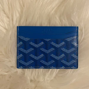 Blå Goy4rd plånbok med mönster - Säljer en blå plånbok från Goy4rd med deras ikoniska grafiska mönster i vitt och svart. Plånboken är i smidig modell för kort och är tillverkad i skinn. Kommer med originalask, dustbag och kvitto. Perfekt accessoar för dig som gillar lyxiga detaljer.