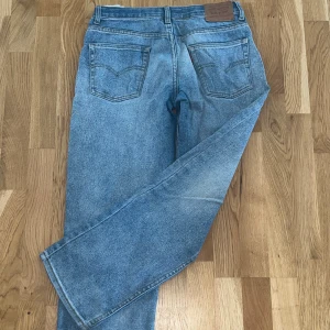 Levi's 501 ljusblå jeans straight fit - Klassiska Levi's 501 jeans i ljusblå tvätt med raka ben och femficksmodell. Jeansen har normal passform, knappgylf och tydlig Levi's-lapp bak i midjan. Perfekta för en avslappnad och tidlös look.